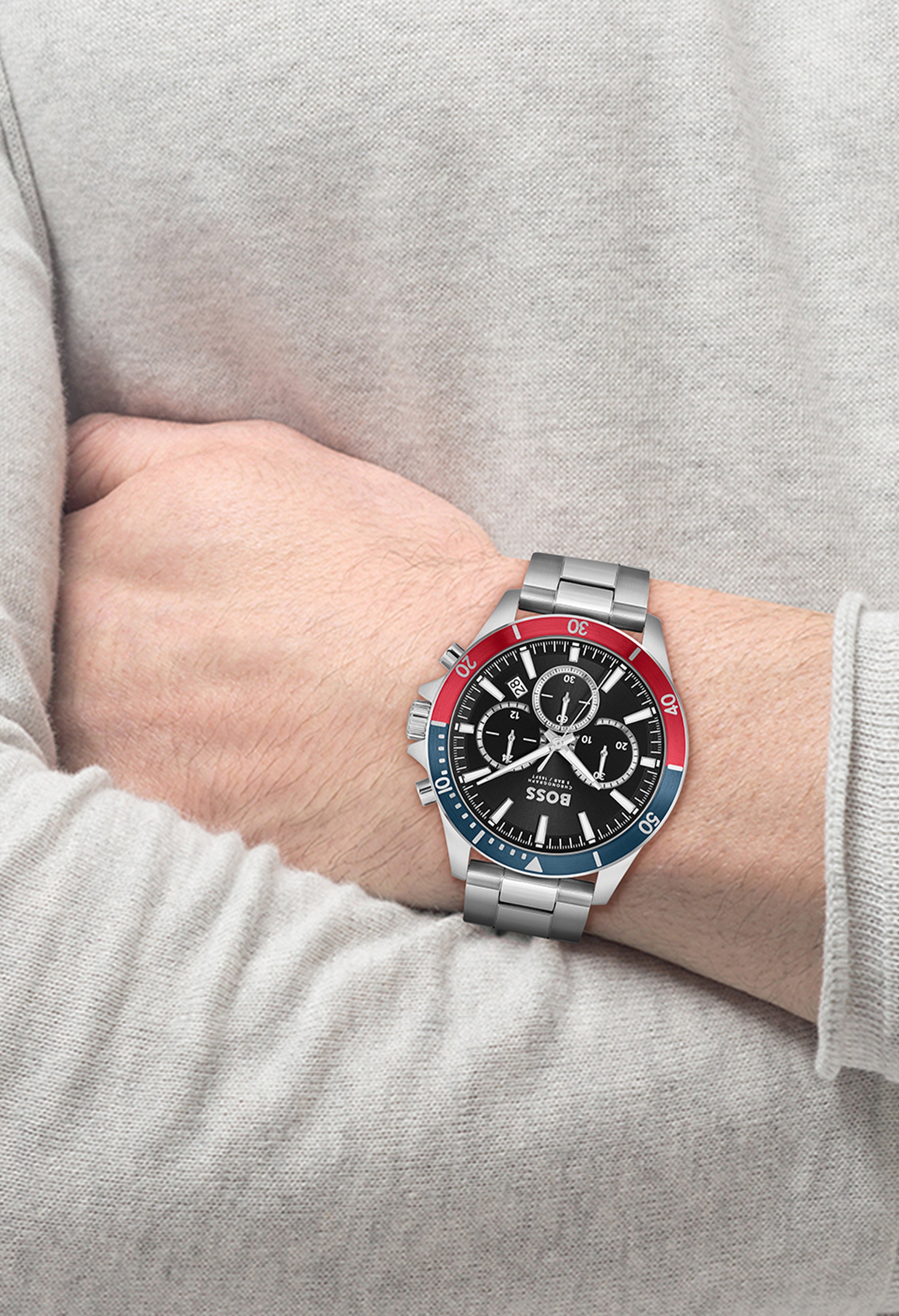 A stainless steel BOSS Troper chronograph watch on a wrist, displaying its black dial and red and blue bezel details.