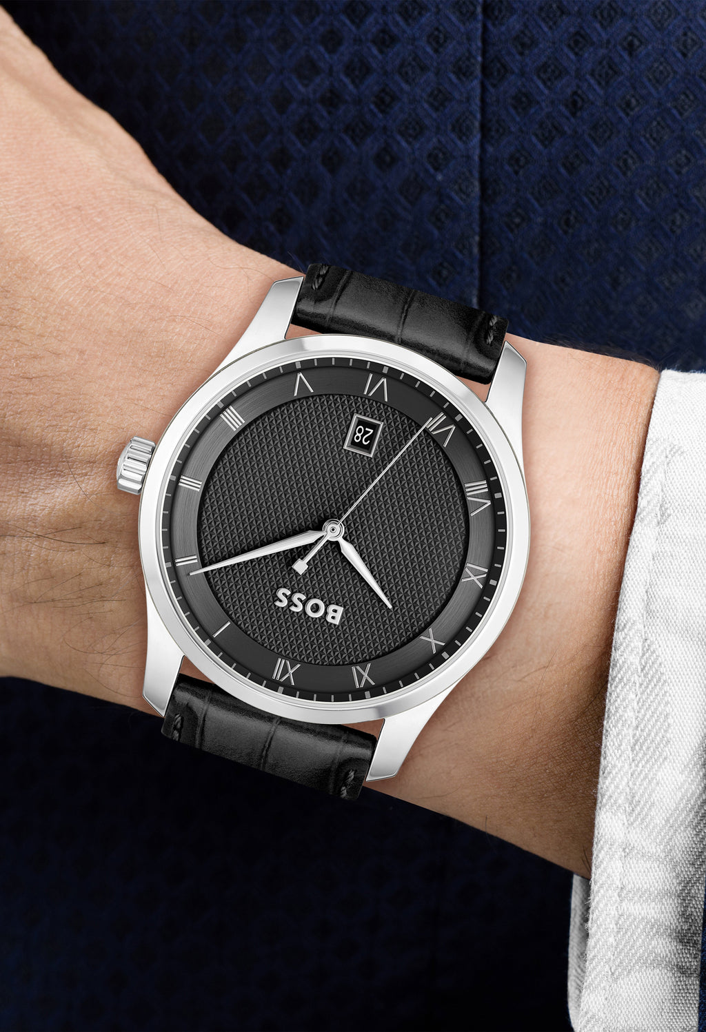 Close-up of a BOSS watch on a wrist, showcasing the black textured dial, stainless steel case, and black leather band.