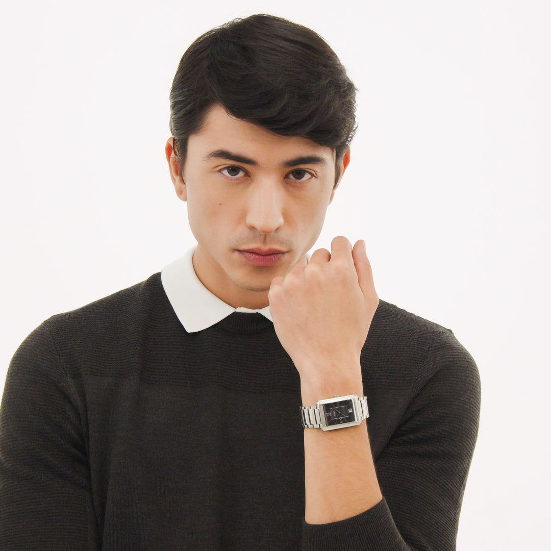 Man in dark sweater with white collar posing with silver wristwatch.
