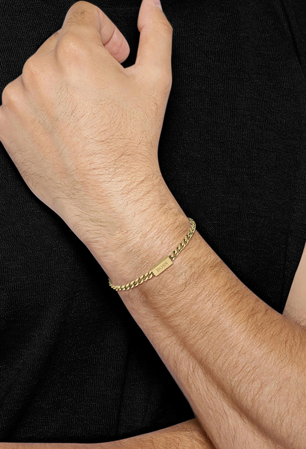 Men's BOSS yellow gold plated chain bracelet. Close-up showcasing bracelet on wrist. Features logo clasp detail.
