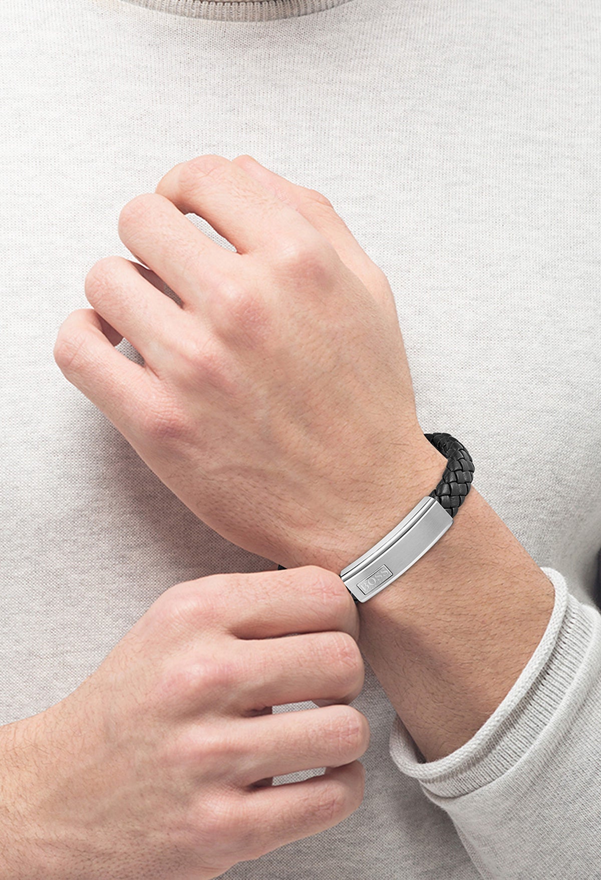 Man fastening a Boss Lander bracelet. The black braided leather strap has a stainless steel cap with the BOSS logo.