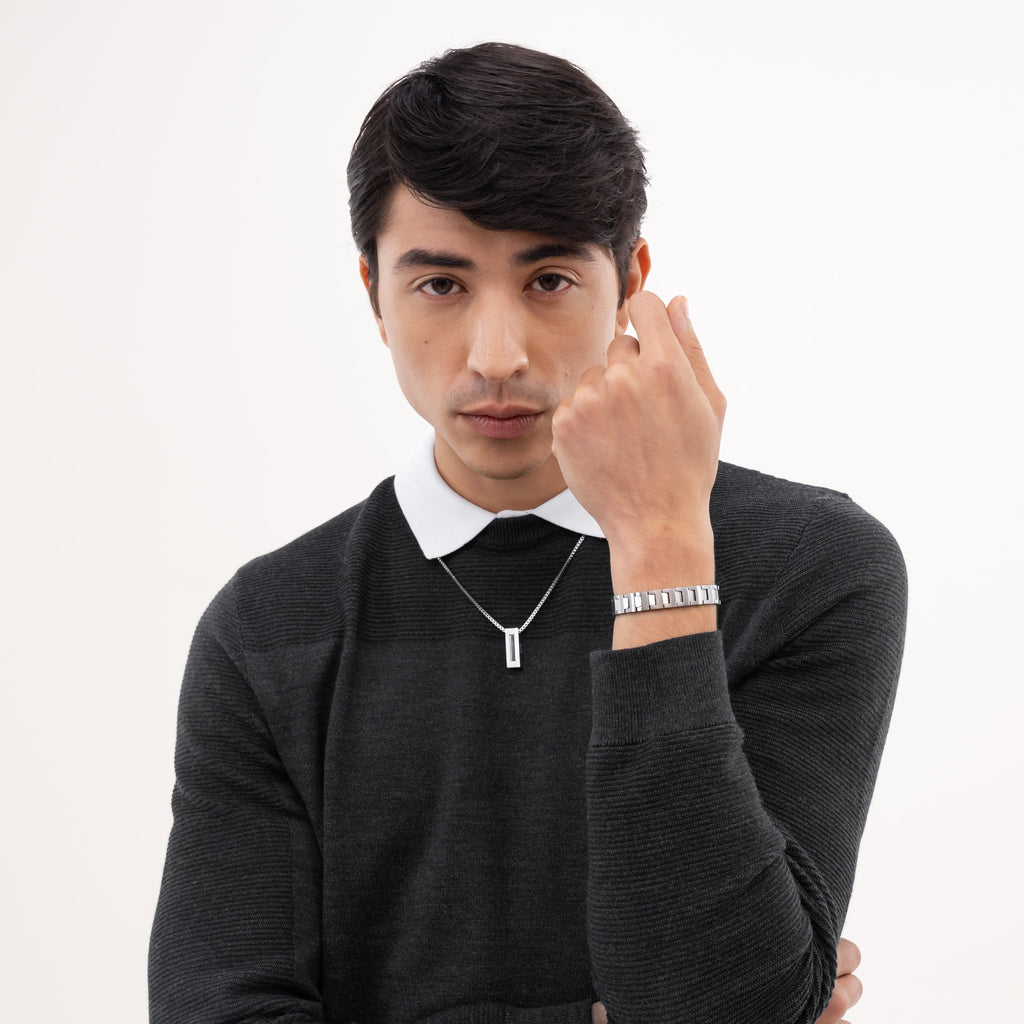 Man in gray sweater and white collared shirt, modeling silver necklace and bracelet.
