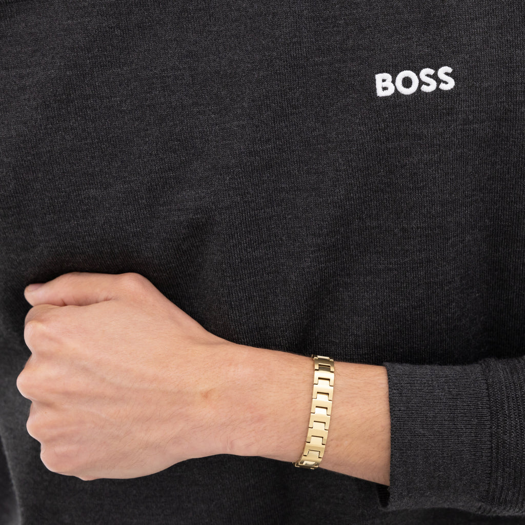 Person wearing a gray sweatshirt with the word "BOSS" and a gold link bracelet.
