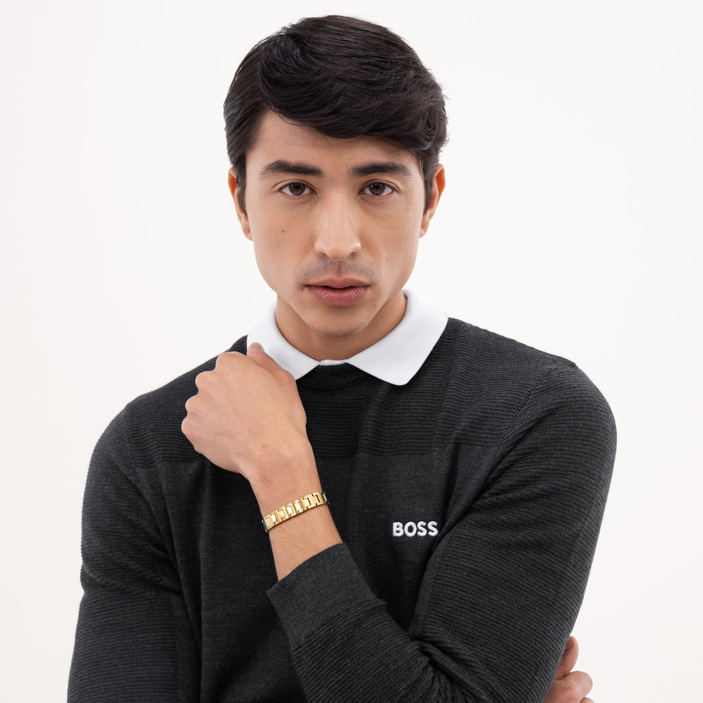 Man in black sweater with white collar and gold bracelet.