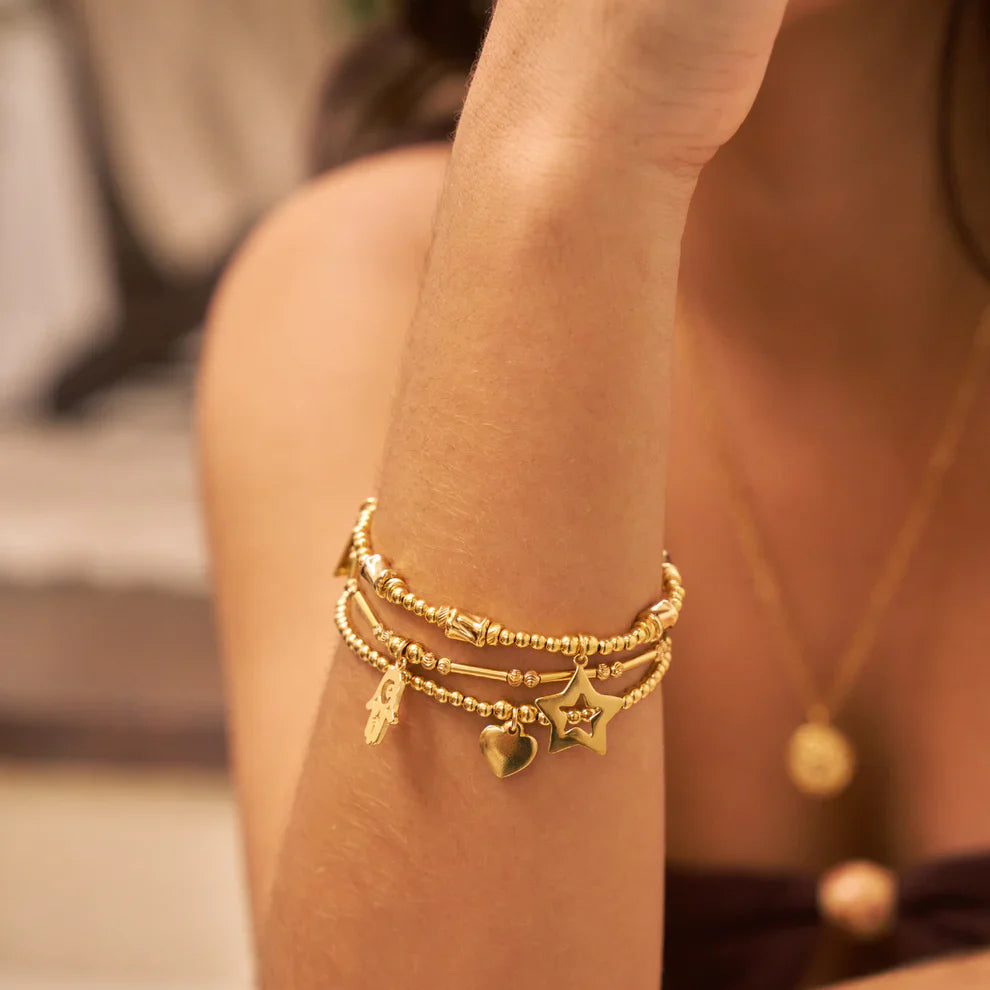 Woman's arm with layered gold beaded charm bracelets, gold pendant necklace.
