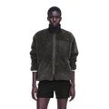A model wearing a dark olive green sherpa zip-up jacket with a black chest pocket and black shorts, photographed against a solid white background.