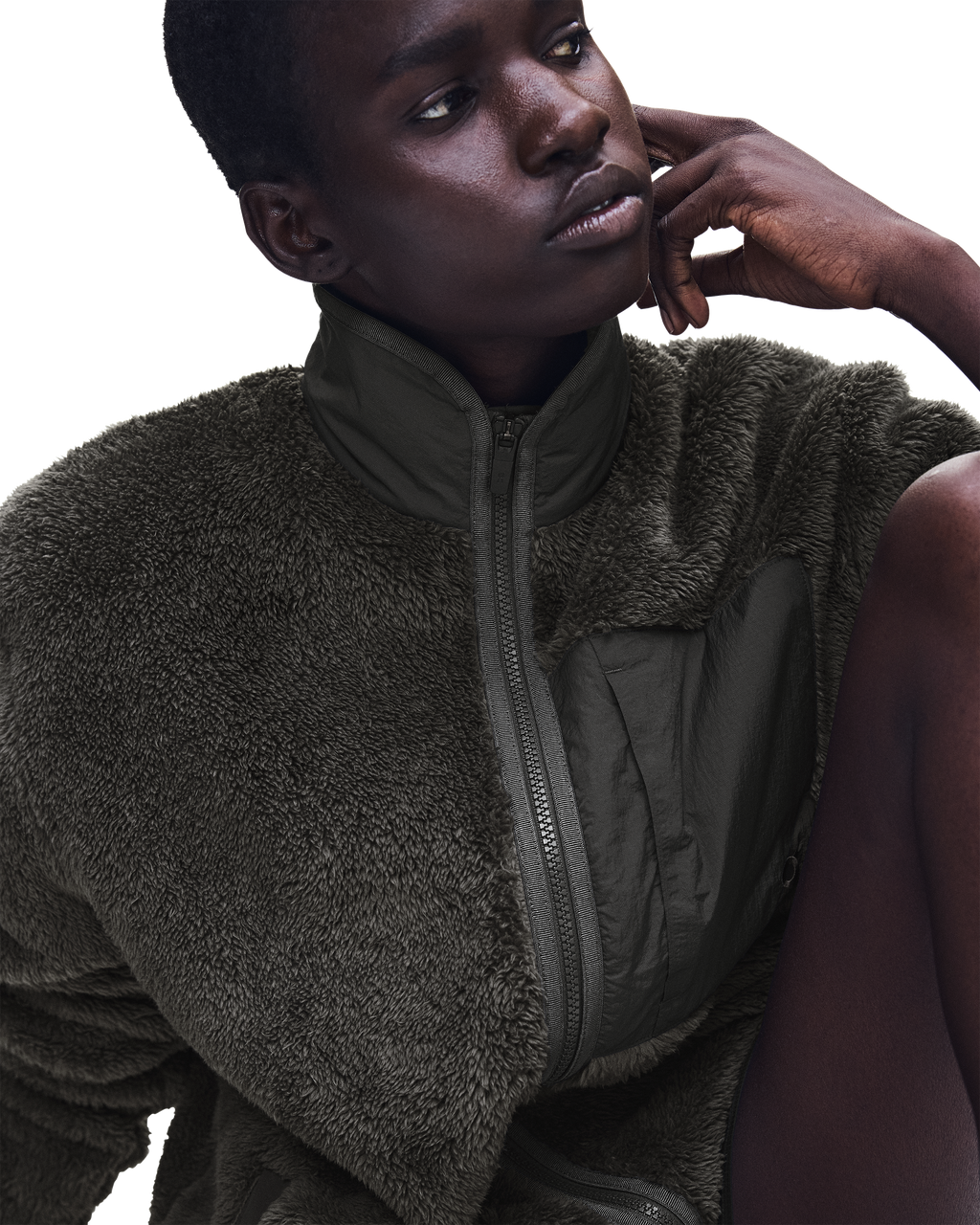 A close-up of a model wearing a dark olive green fleece zip-up jacket with a high collar and a quilted chest panel, set against a solid white background.