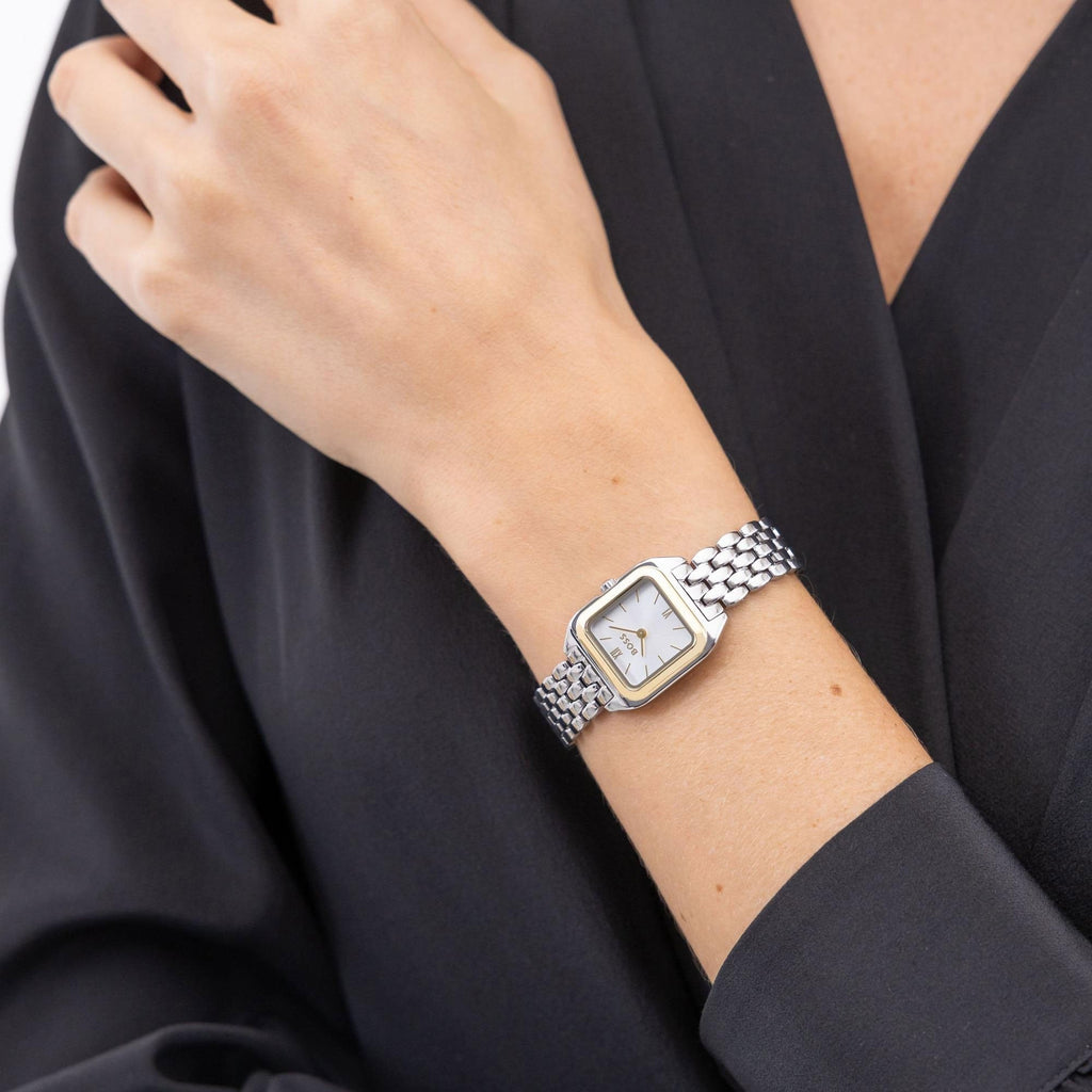 Woman wearing a silver and gold wristwatch with a white face, against a dark colored blouse. 
