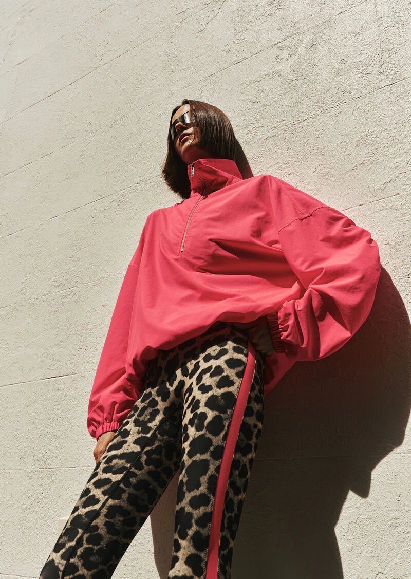 Person wearing a bright pink jacket and leopard print pants against a light gray wall.