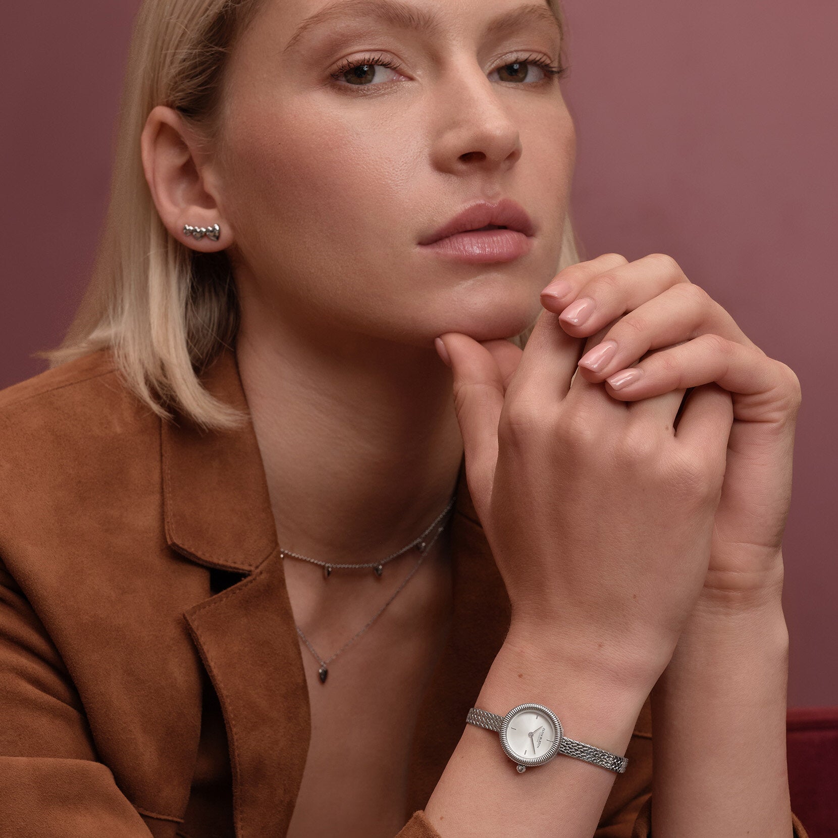Woman wearing silver jewelry and a brown jacket.
