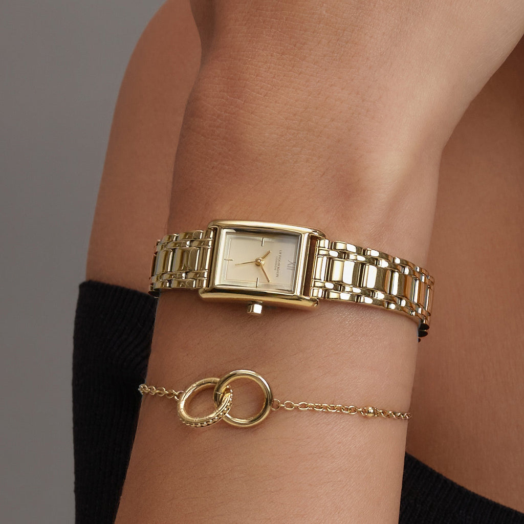 A gold watch and linked circles bracelet on a person's wrist.
