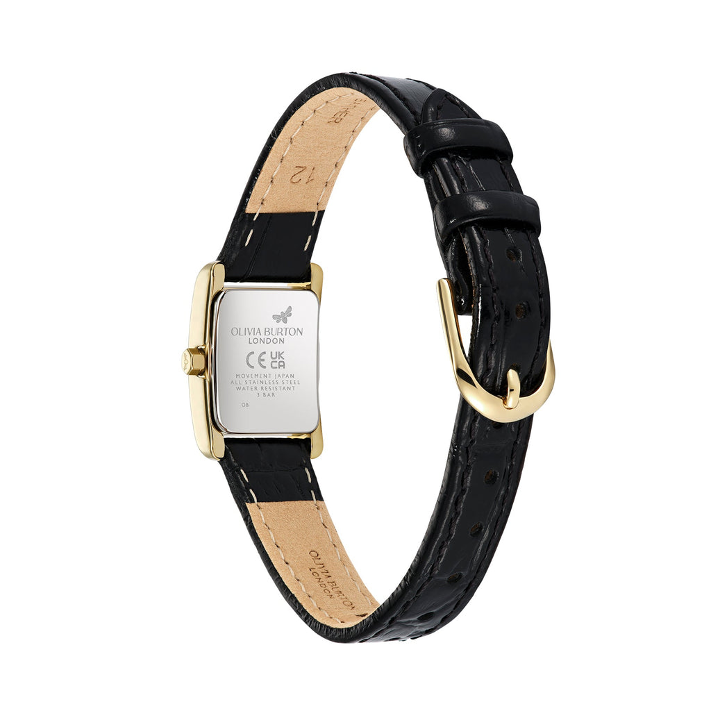 Close-up of the back of an Olivia Burton London wristwatch, featuring a gold-tone rectangular case, a black leather strap with visible stitching, and a gold-tone buckle. The case back has engraved text and symbols, while the strap shows the inner lining and size markings.