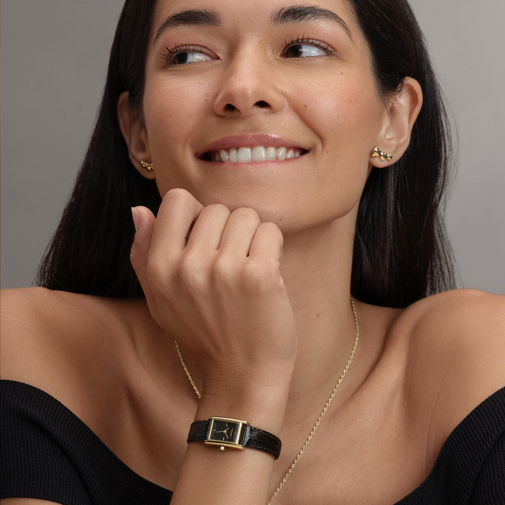 Woman wearing gold jewelry and a black wristwatch.
