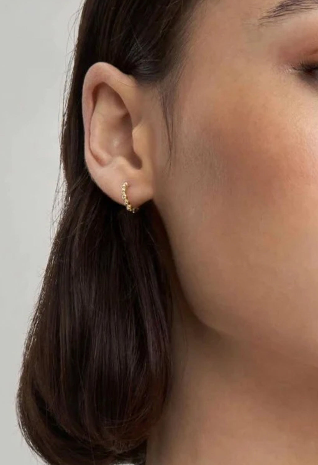 Close-up of a woman's ear wearing Nomination Lovecloud mini hoop earrings in gold plating. Showcases jewelry detail.