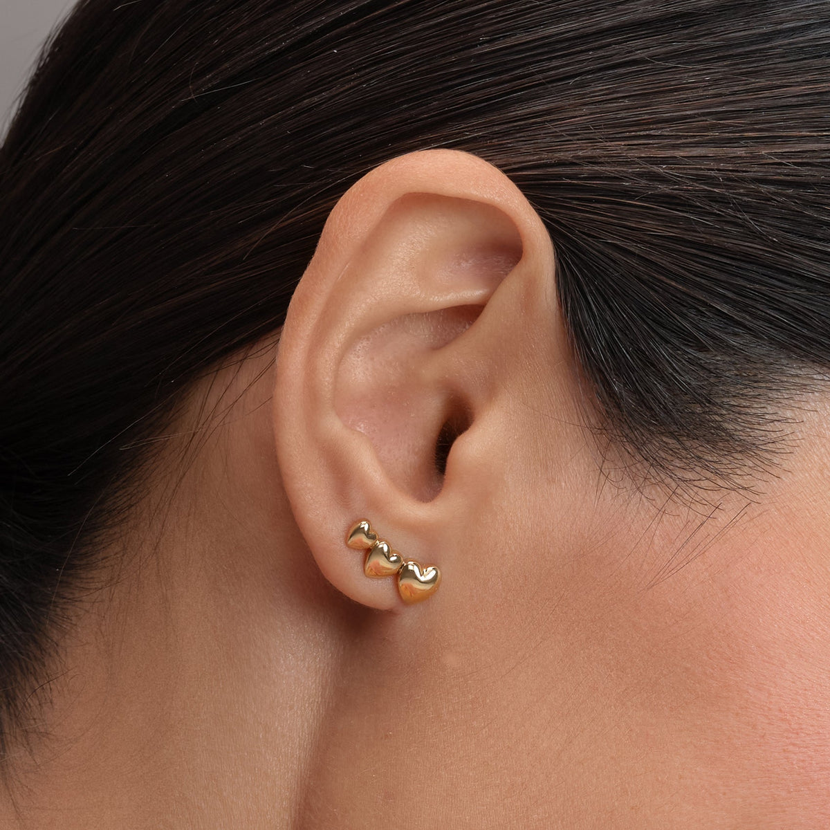 A woman's ear with a gold triple heart stud earring.