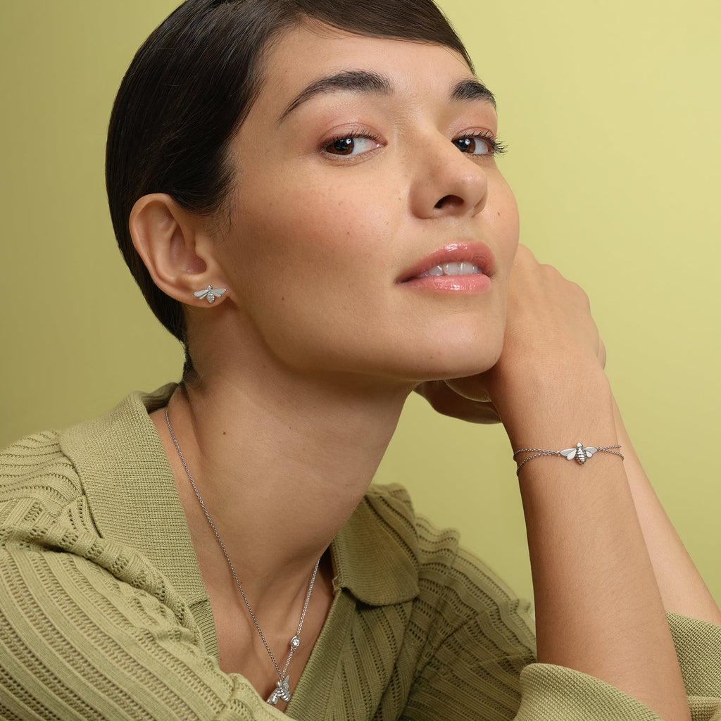 Woman wearing silver bee jewelry, light green top, yellow background.