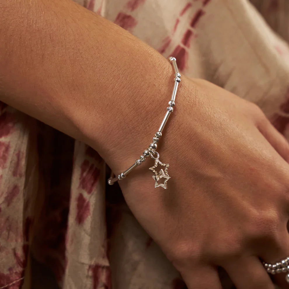 Woman's arm wearing a silver bracelet with a star charm.
