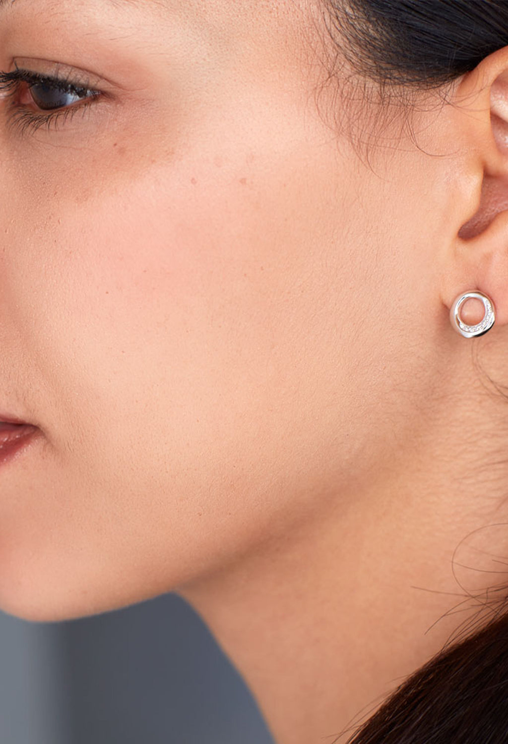 Close-up of a woman wearing Kit Heath silver stud earrings, showcasing the Bevel Cirque design with pave CZ detail.