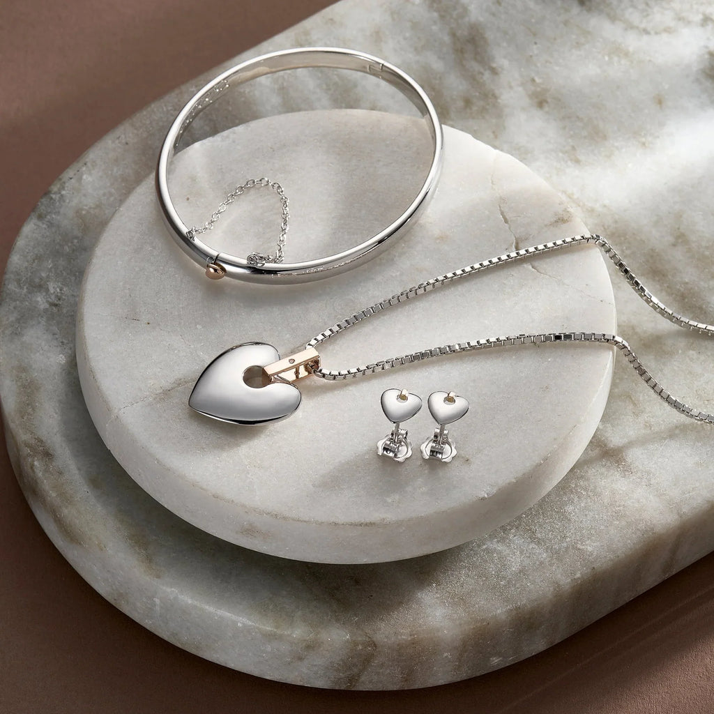 Silver heart jewelry set including a bangle, pendant necklace, and heart-shaped earrings.