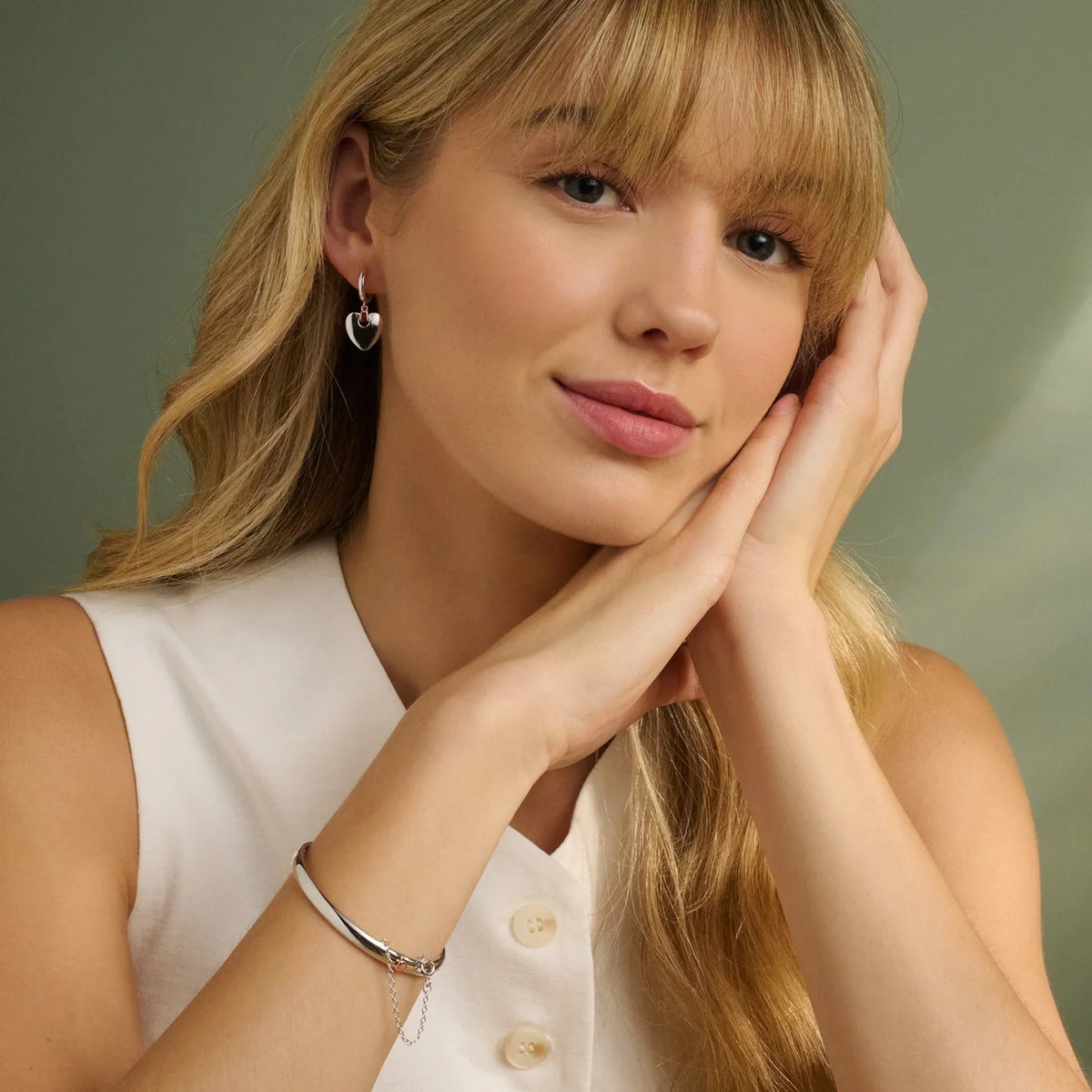 Blonde woman wearing heart earrings and a silver bracelet.