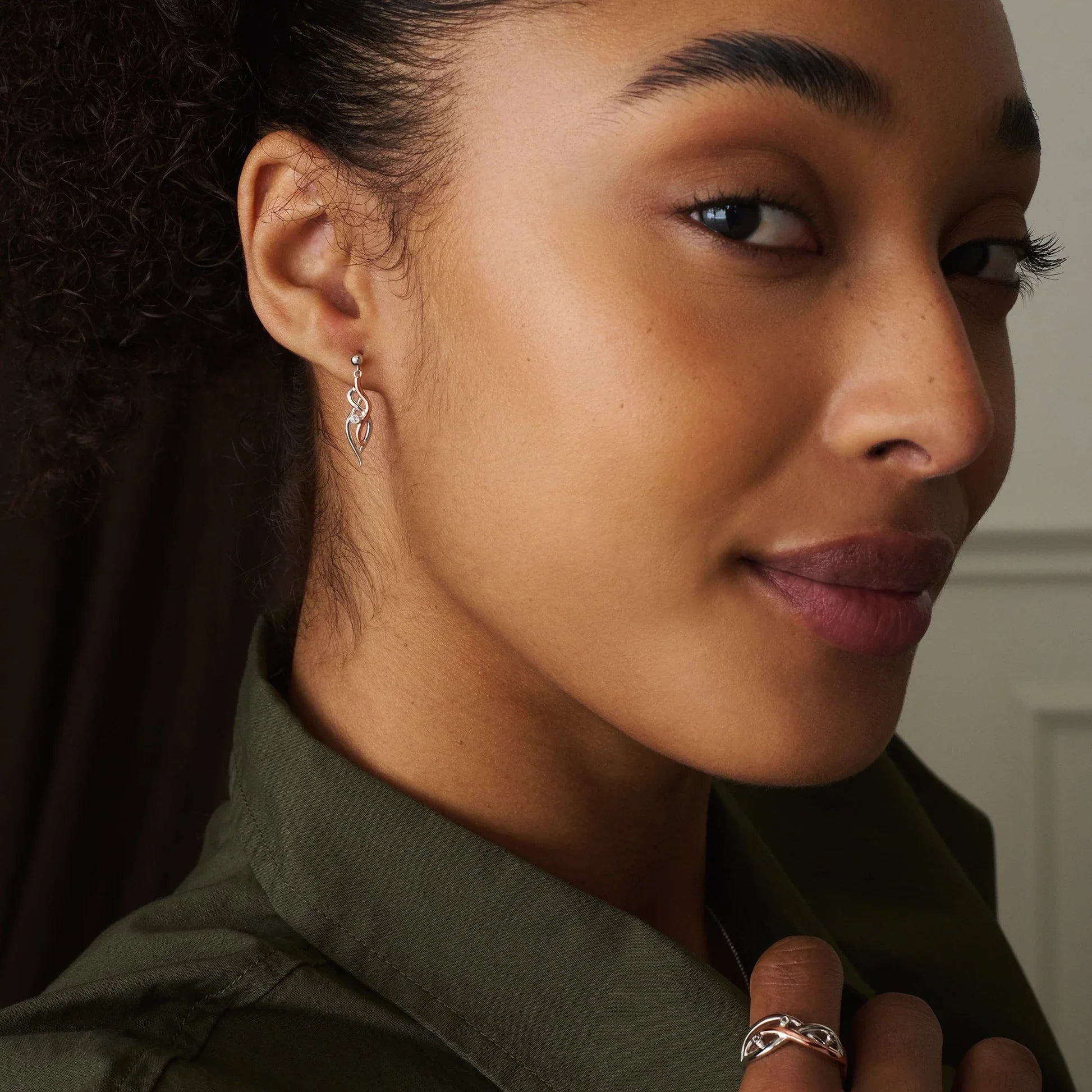Woman wearing silver earrings and ring, green shirt, looking at camera.