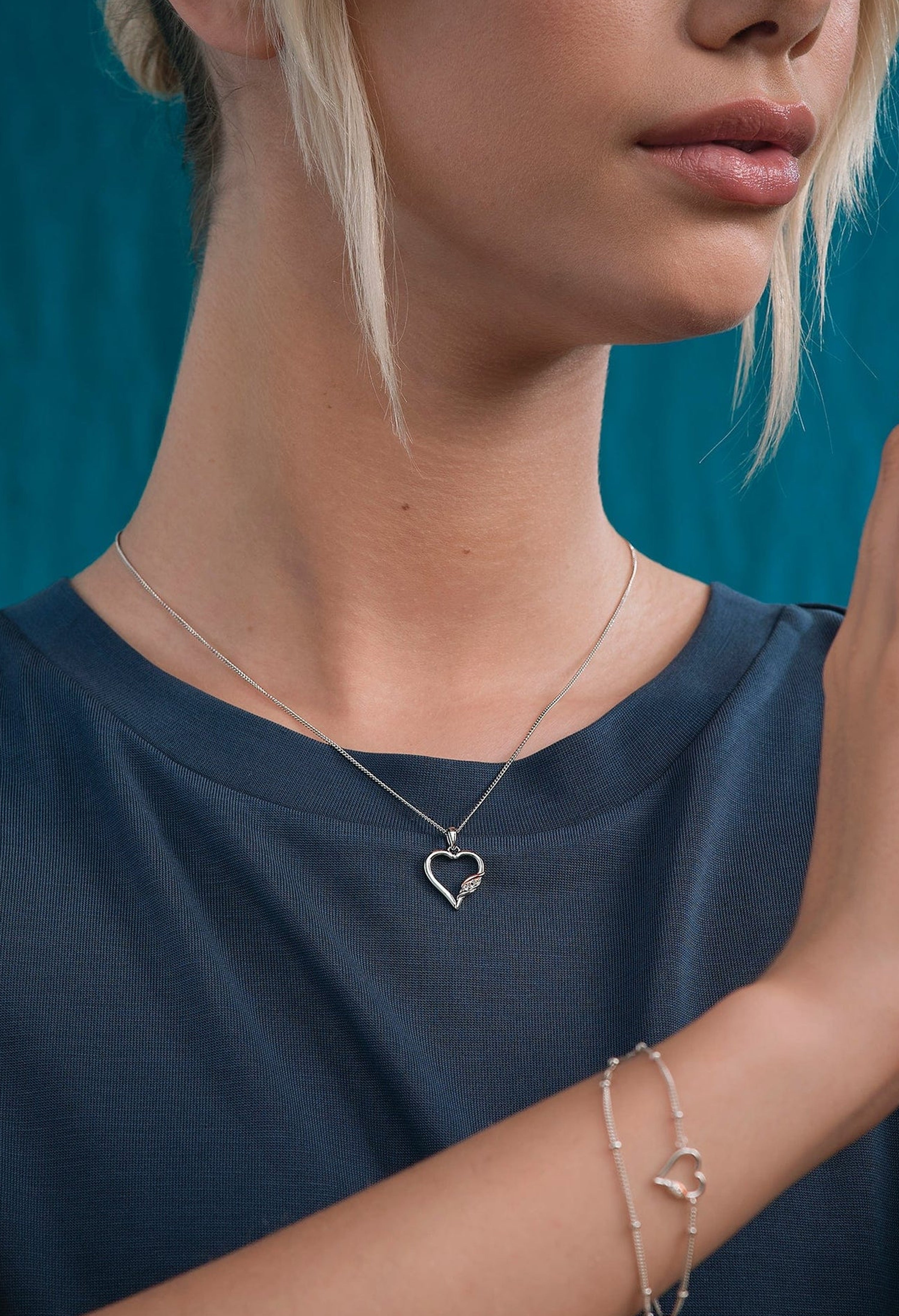 Woman wearing a Clogau heart pendant necklace in silver with white topaz detail. Elegant jewelry.