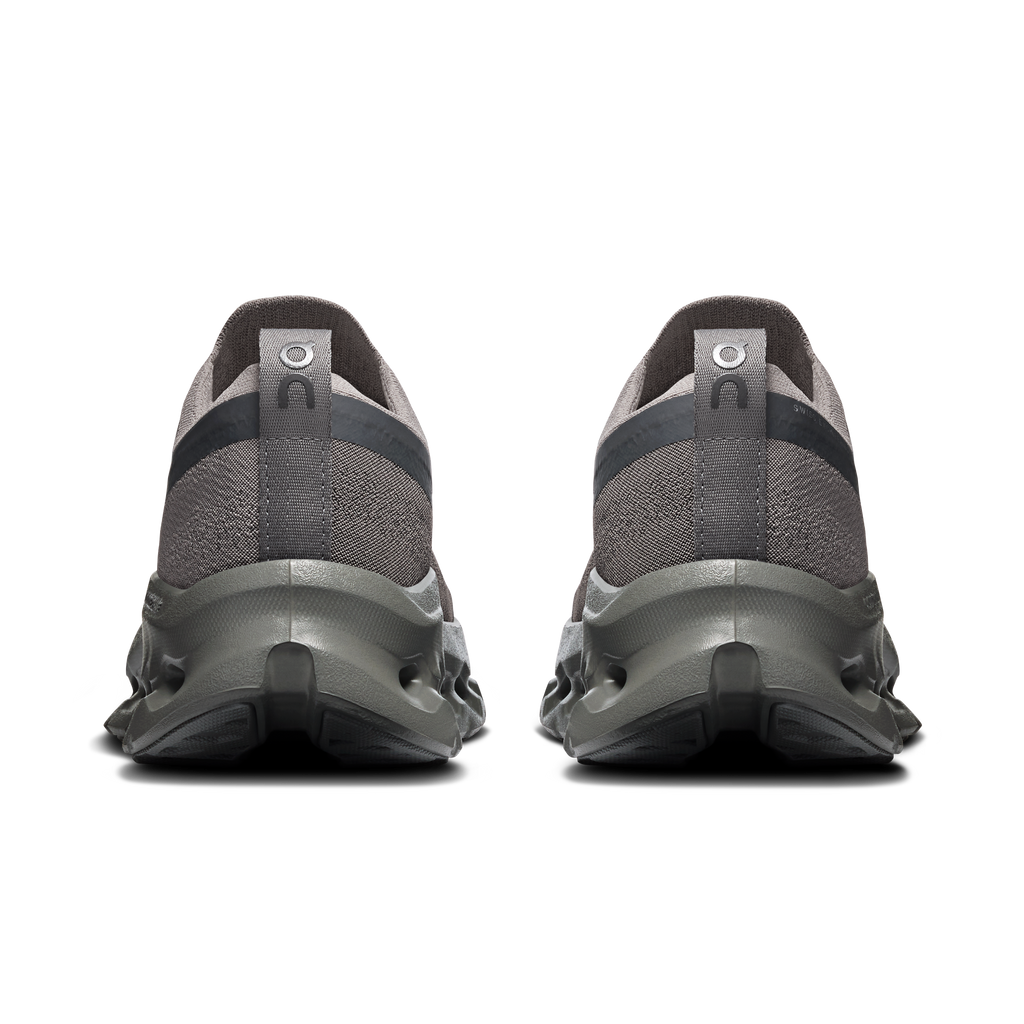 A pair of dark gray and black athletic sneakers shown from the rear, featuring textured knit uppers and chunky sculpted midsoles, set against a plain white background.