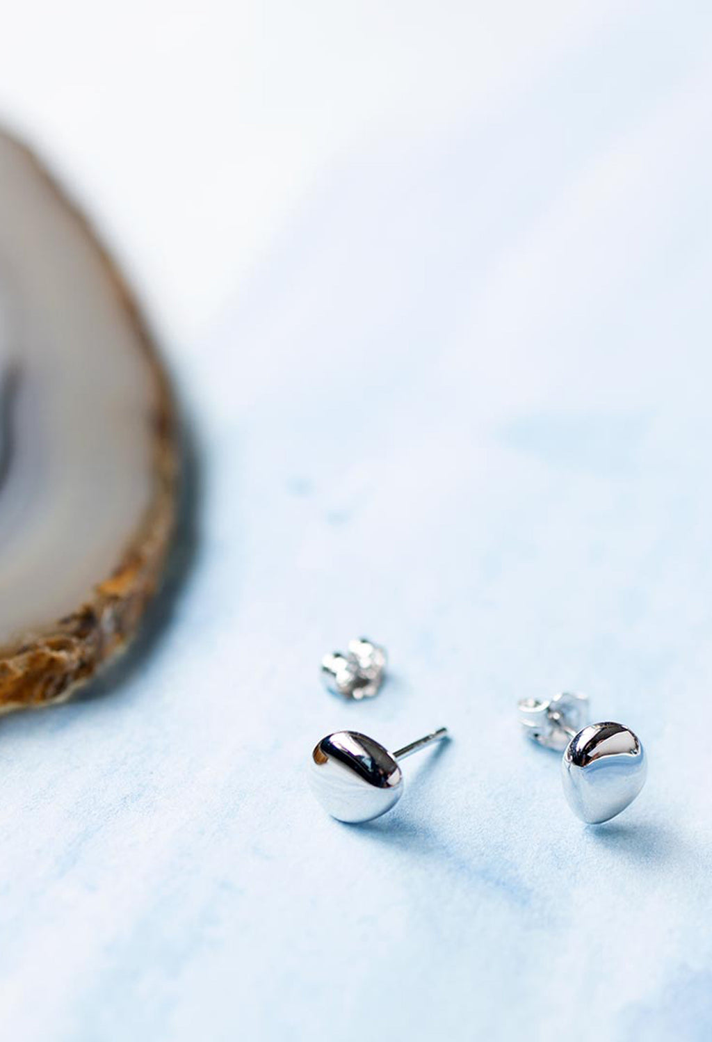 Close-up showing Kit Heath Coast Pebbles silver stud earrings with pebble-shaped design, showcasing fine jewelry detail.