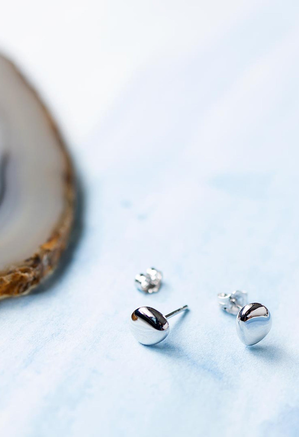 Close-up showing Kit Heath Coast Pebbles silver stud earrings with pebble-shaped design, showcasing fine jewelry detail.