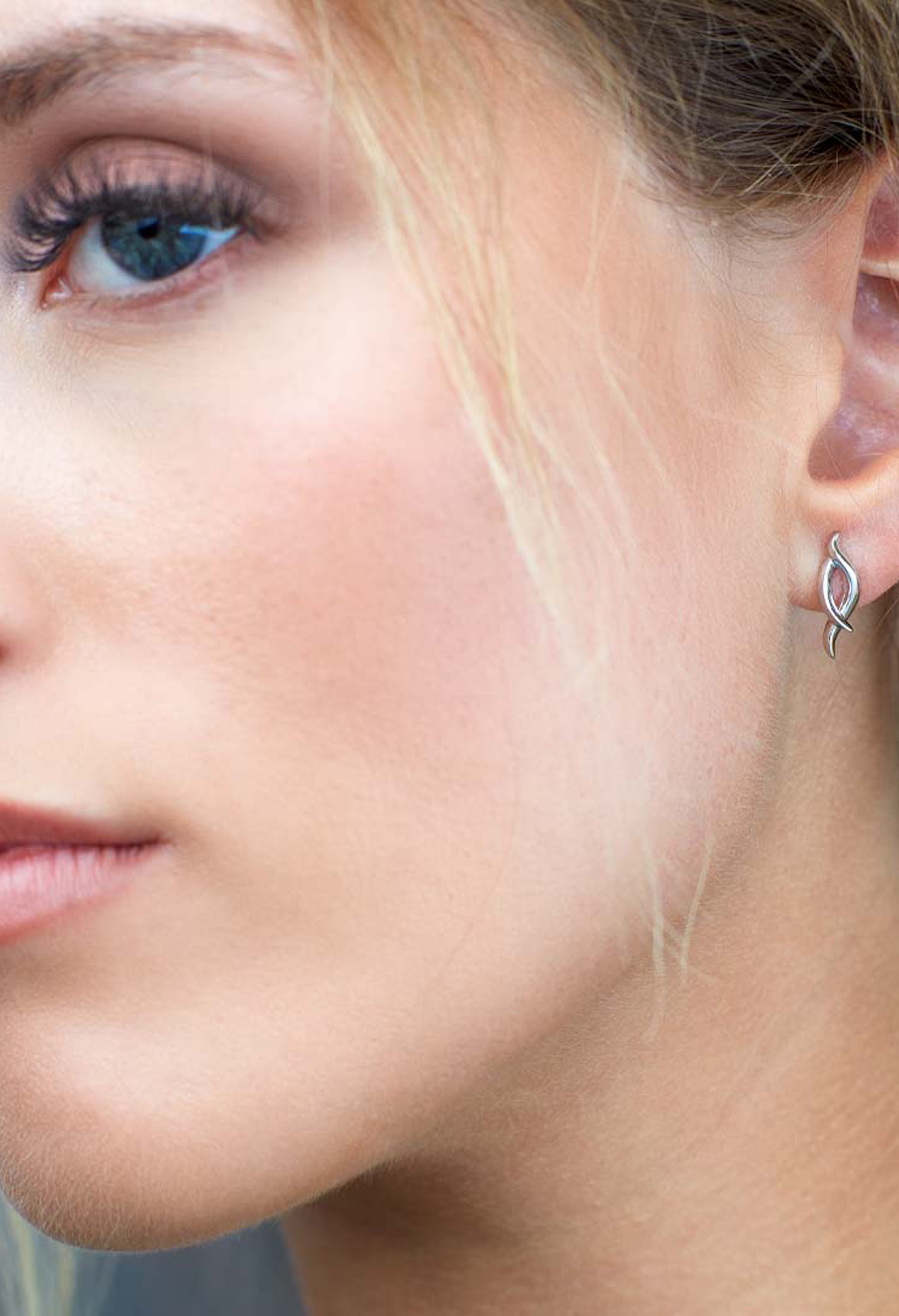 Close-up of a woman wearing the Kit Heath Entwine Twine Twist Stud Earrings, showcasing earring design and fit.