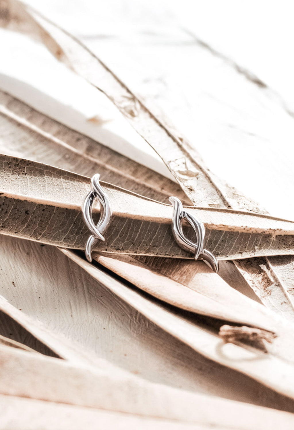 Silver Kit Heath twist stud earrings displayed on decorative leaves, showcasing jewelry design detail.