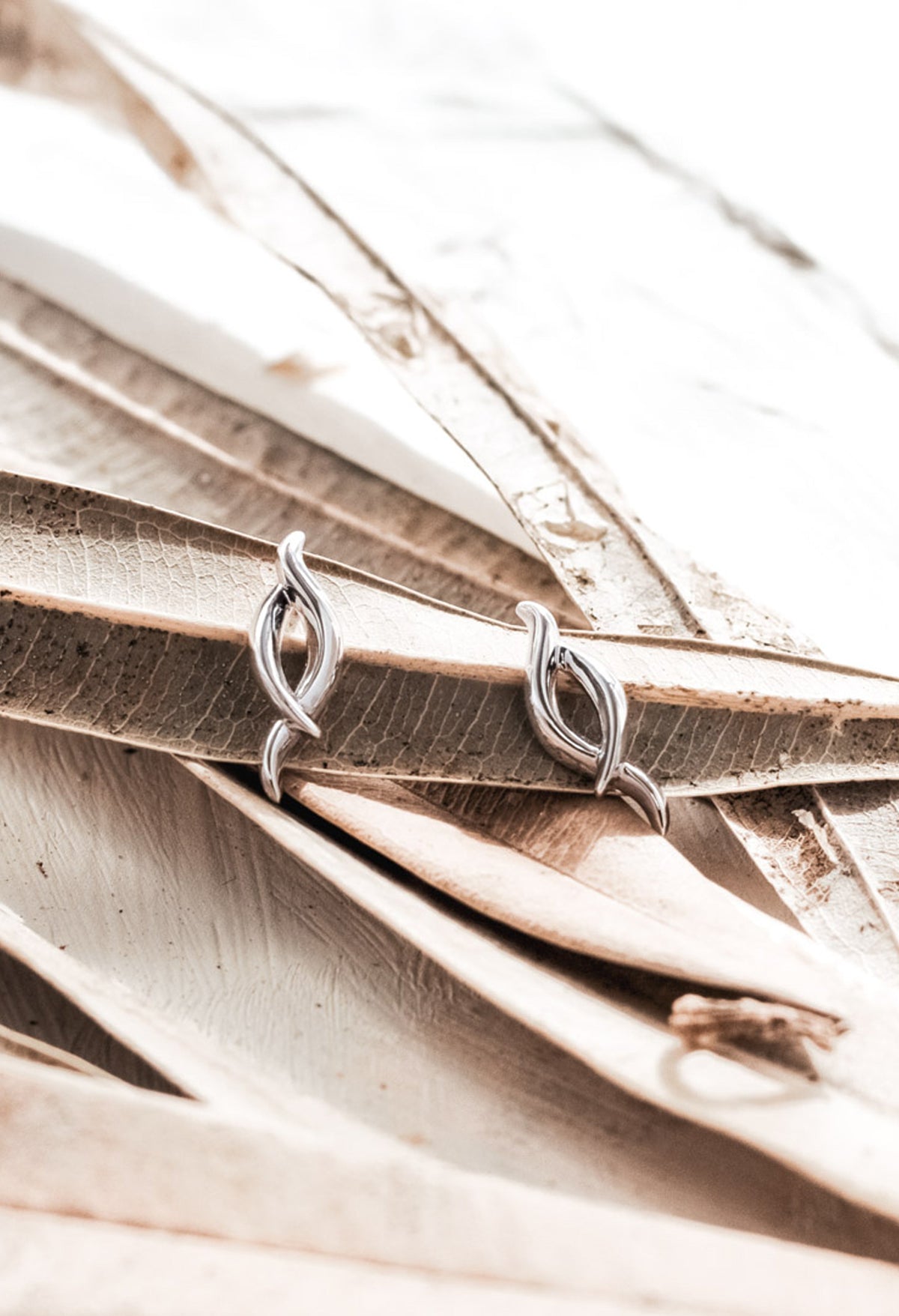 Silver Kit Heath twist stud earrings displayed on decorative leaves, showcasing jewelry design detail.