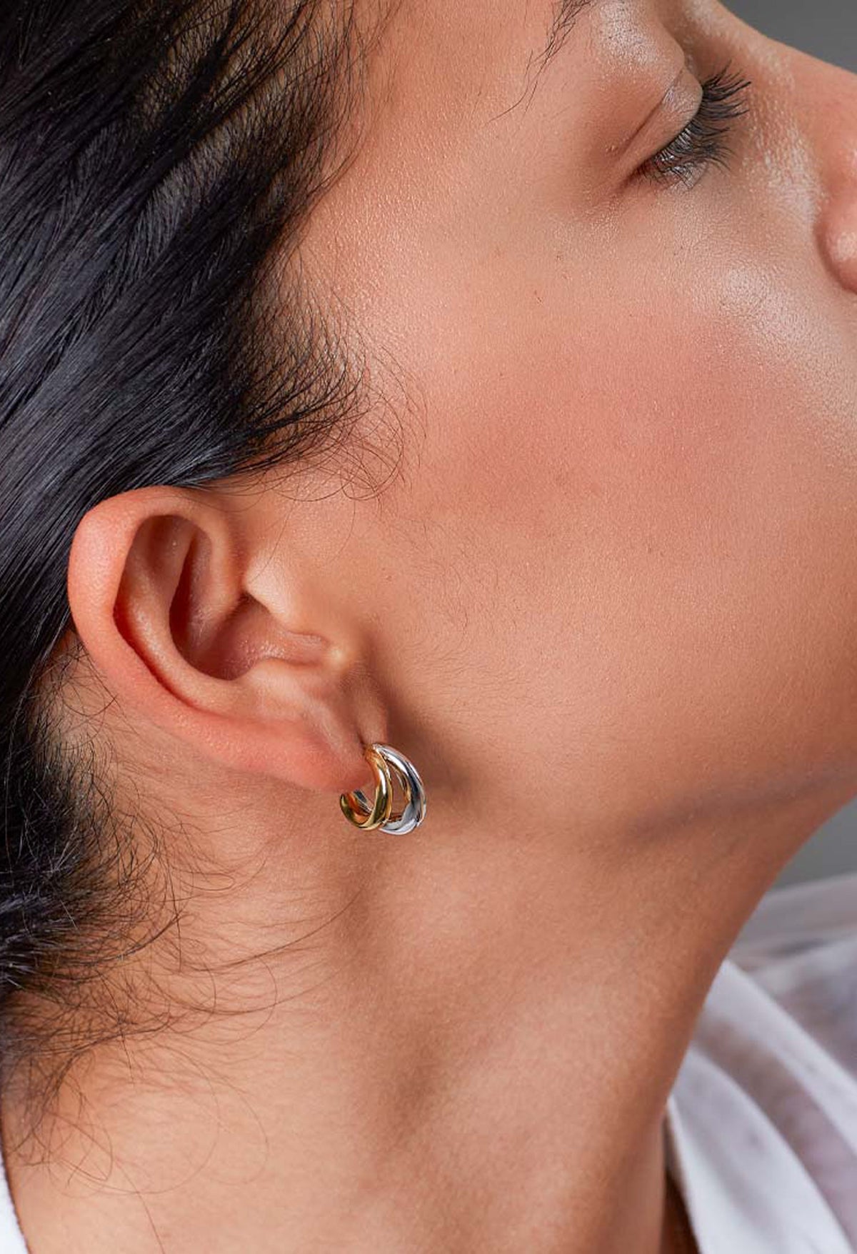 Close-up of Kit Heath Bevel Cirque Link Twin Hoop Earrings in silver and gold, worn on ear. Jewelry detail.