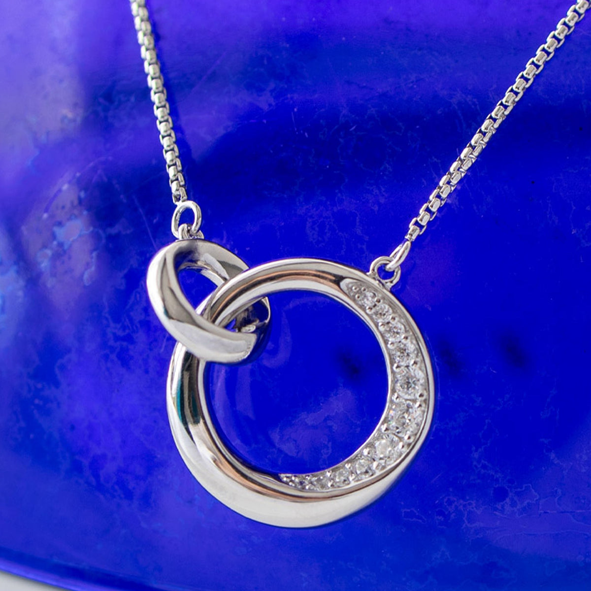 Silver necklace featuring a linked circle pendant, partially pave set with cubic zirconia stones. Bevel Cirque design,