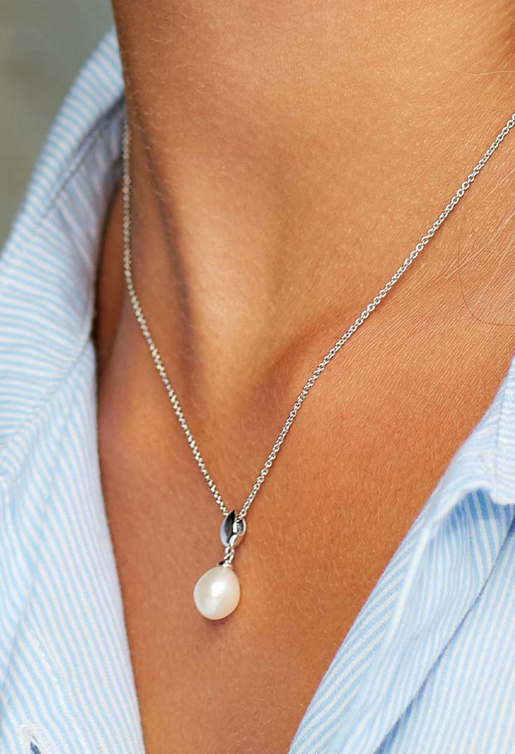 Woman wearing a Kit Heath pearl necklace. Elegant Coast Pebble pearl pendant on a delicate sterling silver chain.