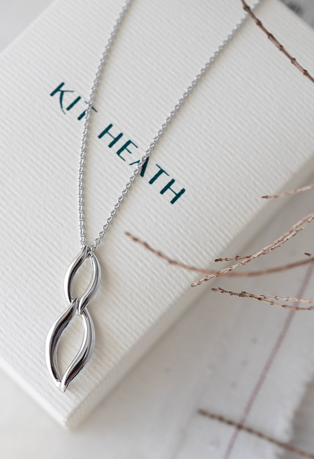 Kit Heath Entwine silver necklace on gift box. Classic designer jewelry showcased for online retail with "KIT HEATH"