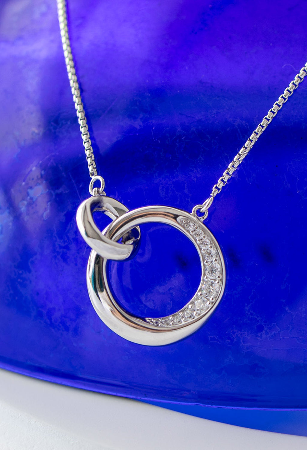 Silver necklace featuring a linked circle pendant, partially pave set with cubic zirconia stones. Bevel Cirque design,