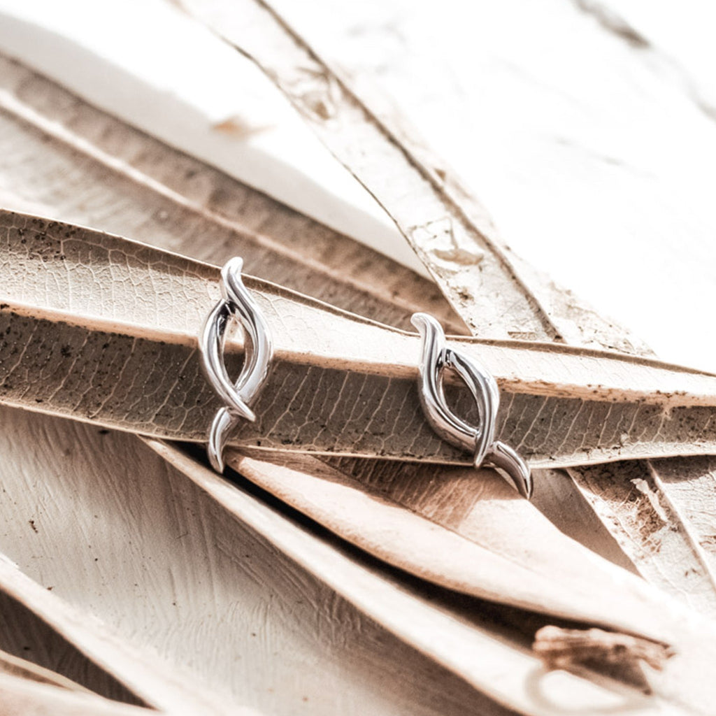 Silver Kit Heath twist stud earrings displayed on decorative leaves, showcasing jewelry design detail.