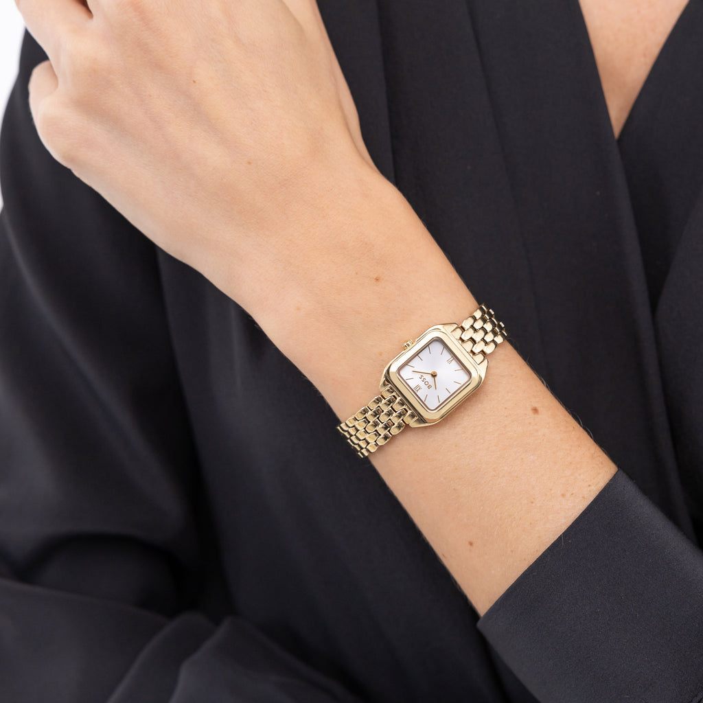 Woman's wrist with gold watch, black dress.
