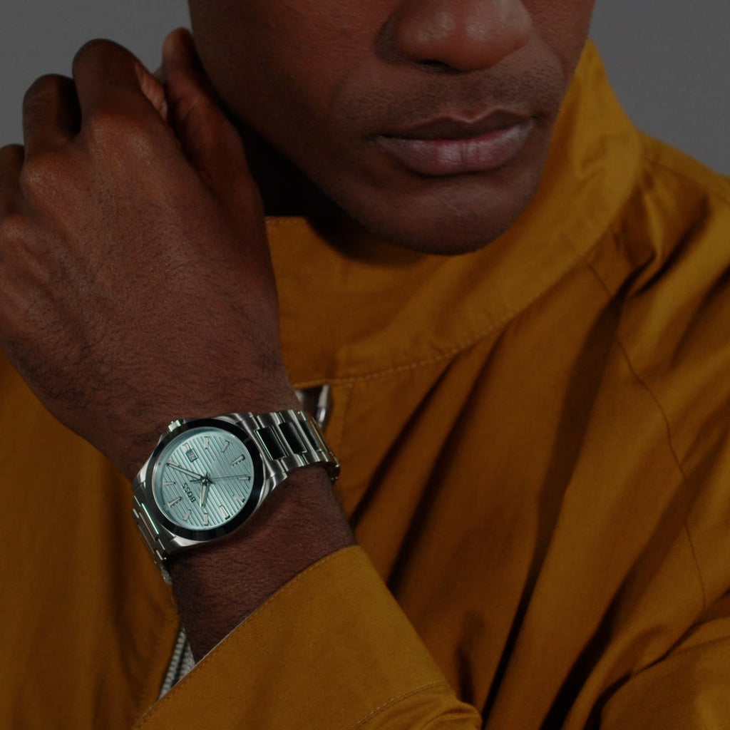 Man wearing Boss Strike watch showcasing its turquoise dial and stainless steel bracelet on wrist.