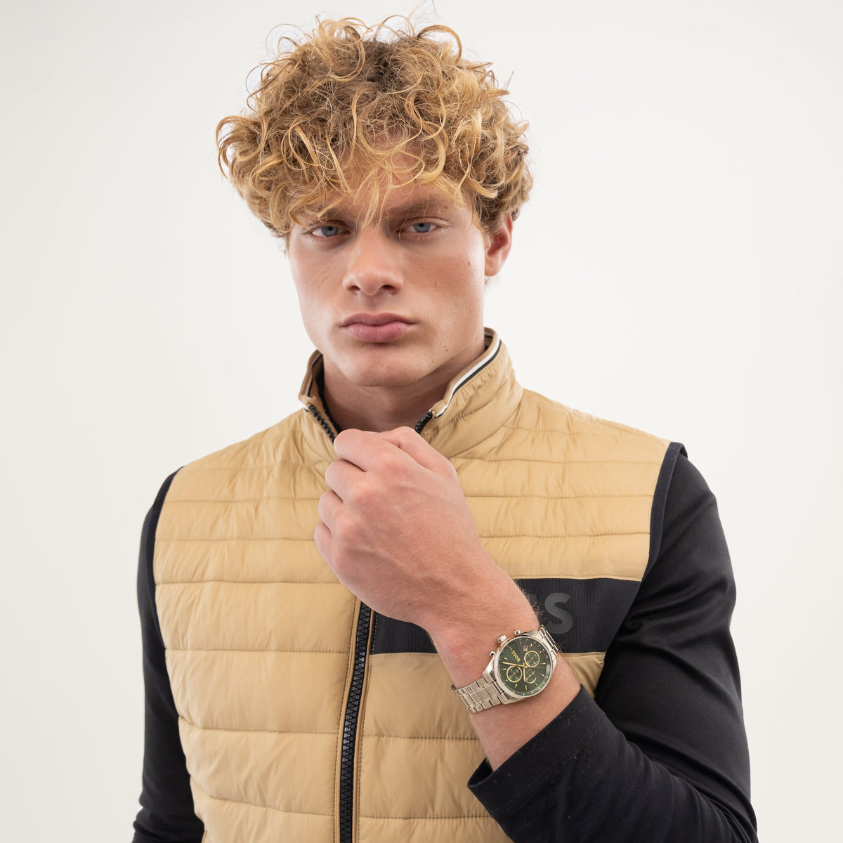 Man wearing a tan puffer vest over a black long-sleeve shirt, posing with a wristwatch.