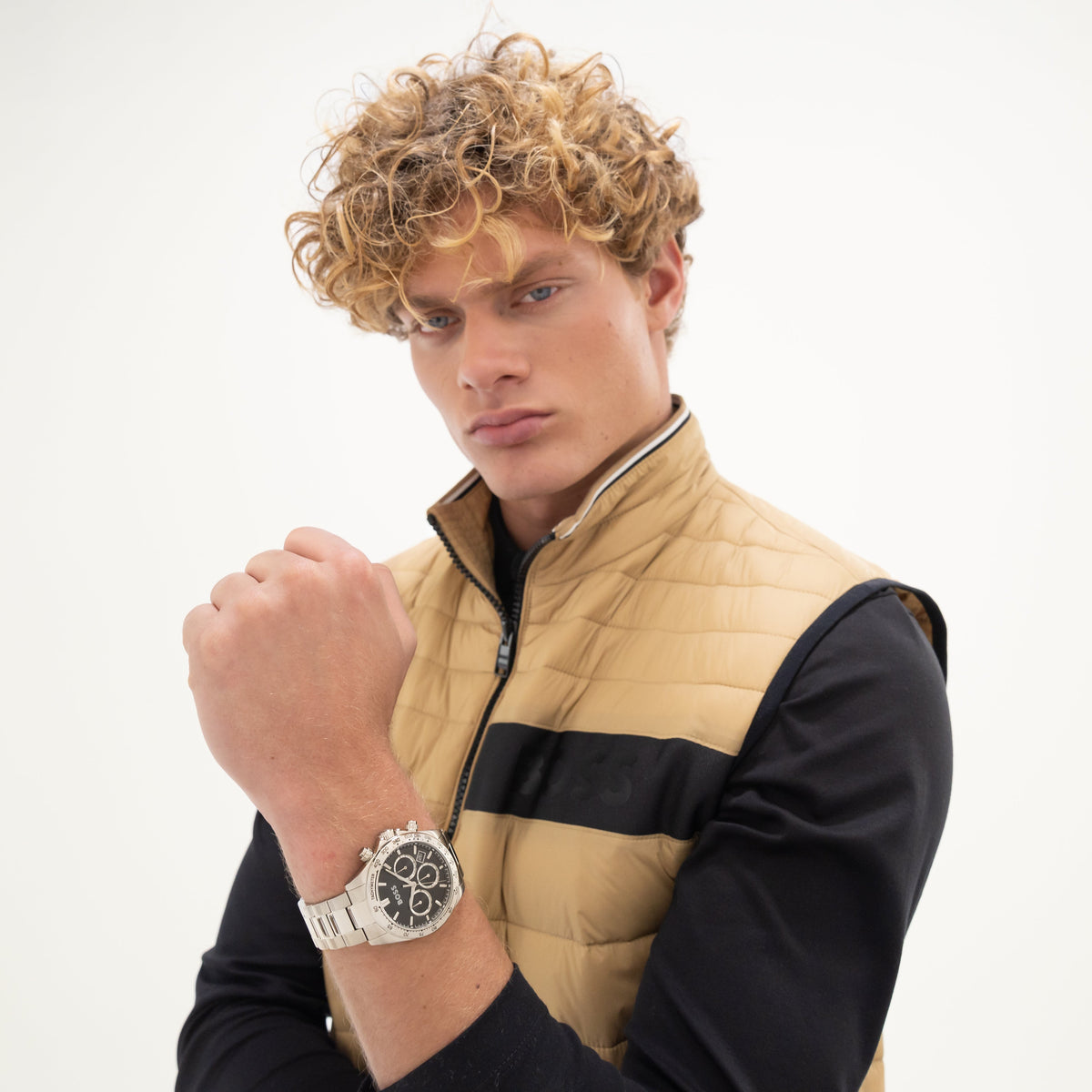 Man in tan puffer vest and black long sleeve shirt with silver watch.