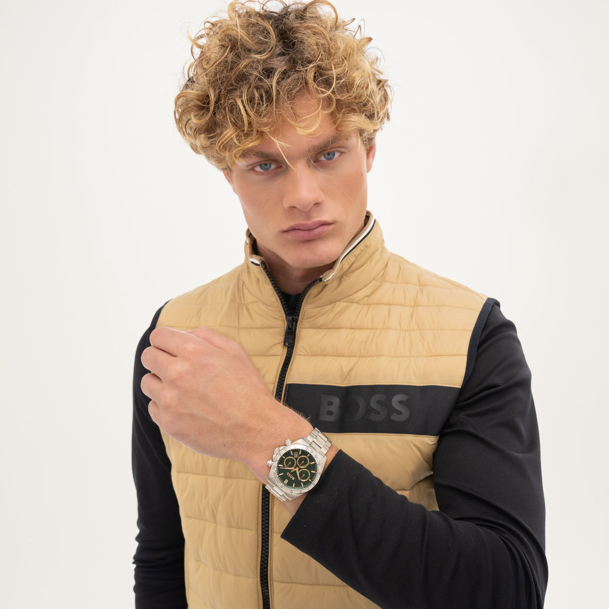 Man wearing a tan vest with the BOSS logo, a black shirt, and a silver watch.