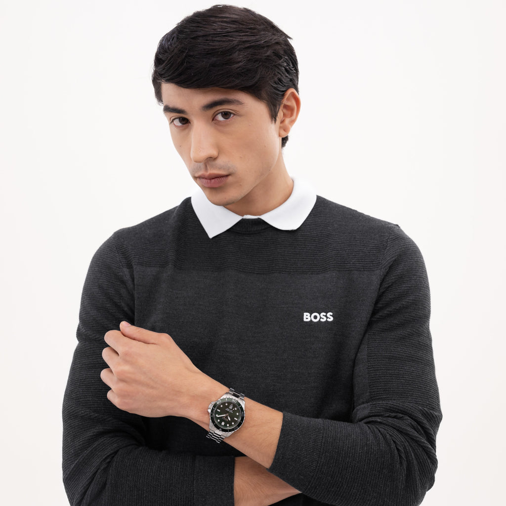 A man in a BOSS gray ribbed sweater with a white collar, posing with his arms crossed, wearing a BOSS watch against a white background.