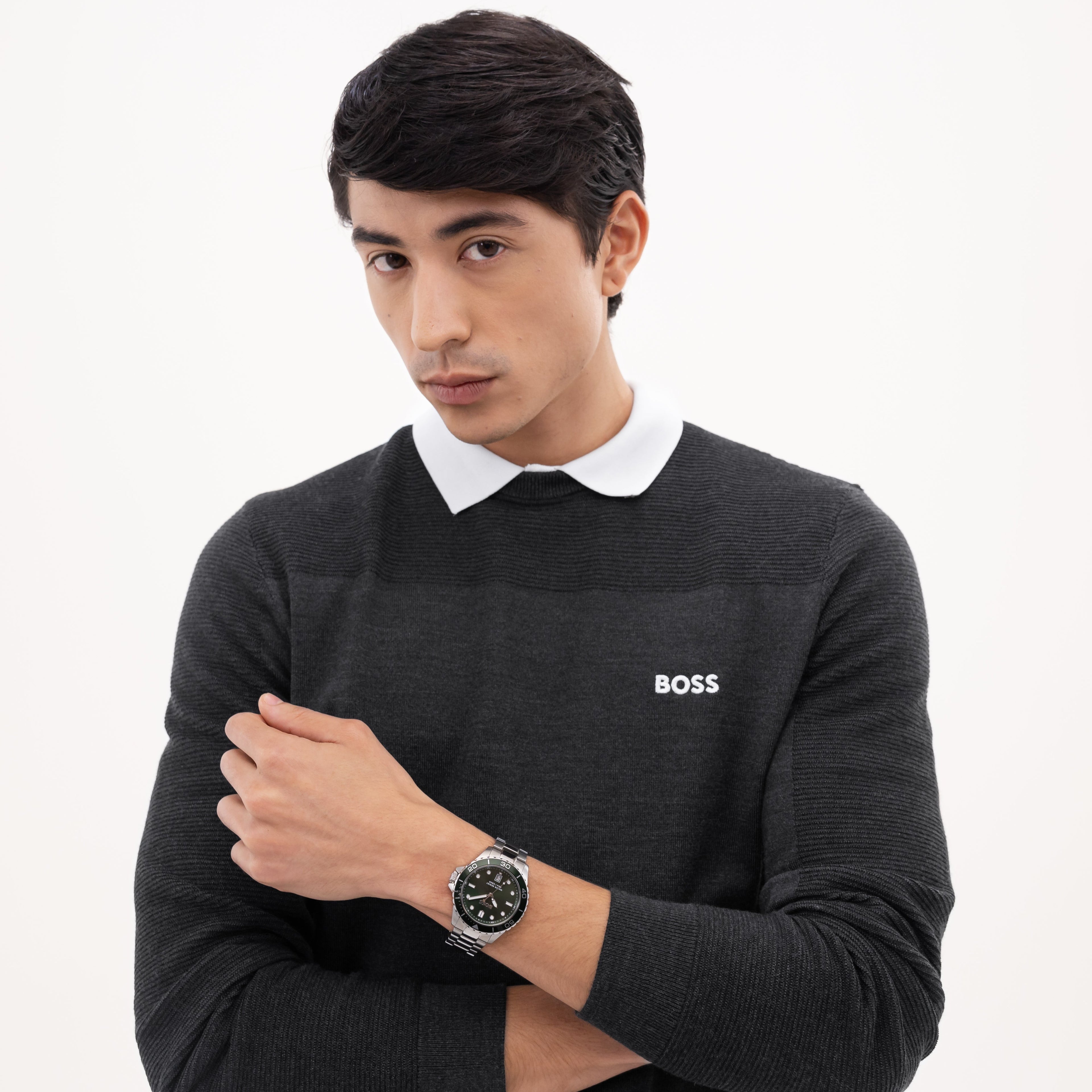 A man in a BOSS gray ribbed sweater with a white collar, posing with his arms crossed, wearing a BOSS watch against a white background.
