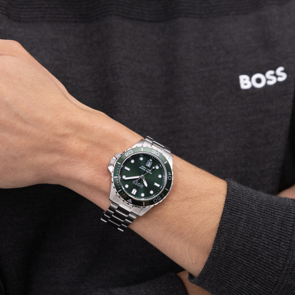 Close-up of a wrist wearing a silver Boss watch with a green face and a dark gray sweater.