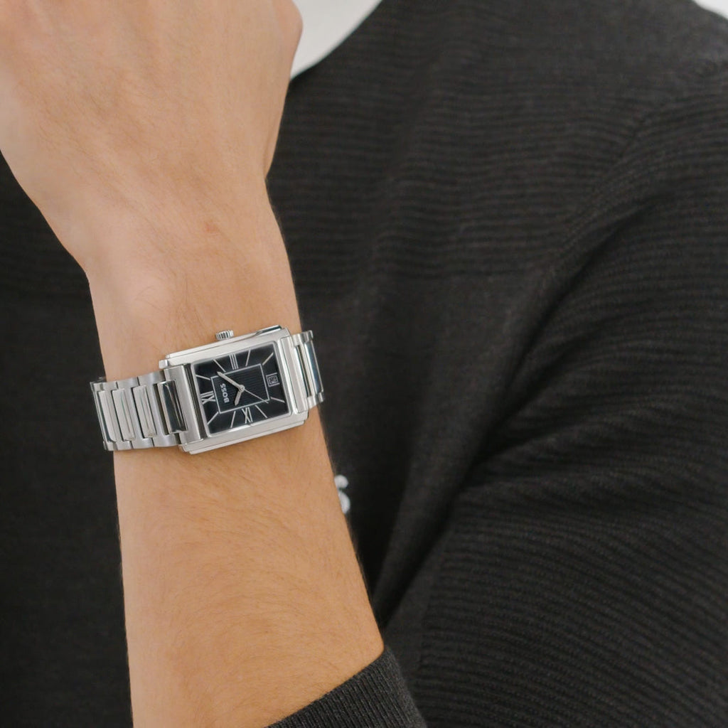 Close-up of a wrist wearing a silver BOSS watch with a black face and date display, against a dark grey knitted sweater.
