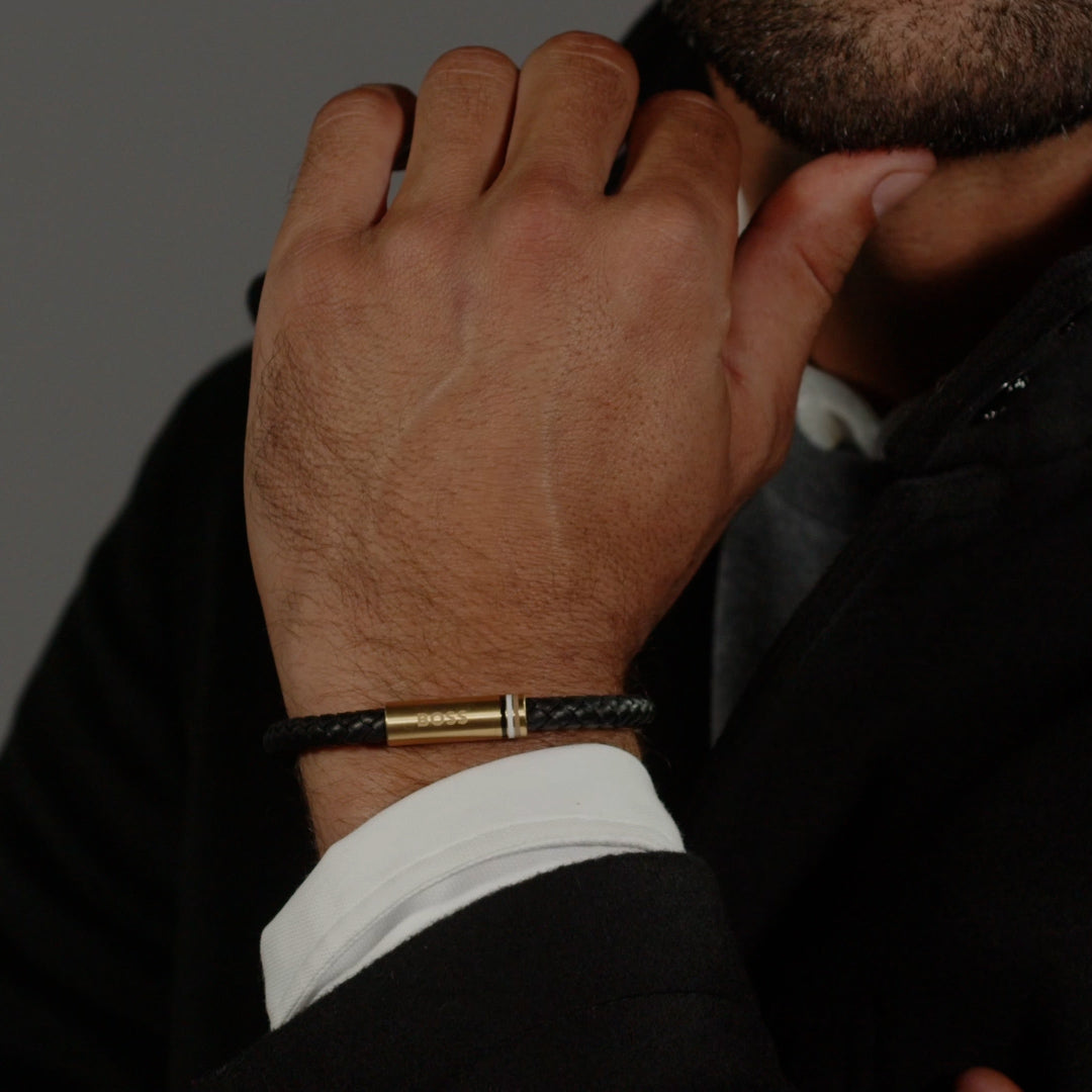 Man wearing Boss braided leather bracelet; gold plated clasp detail with logo, shown with suit and white cuff.
