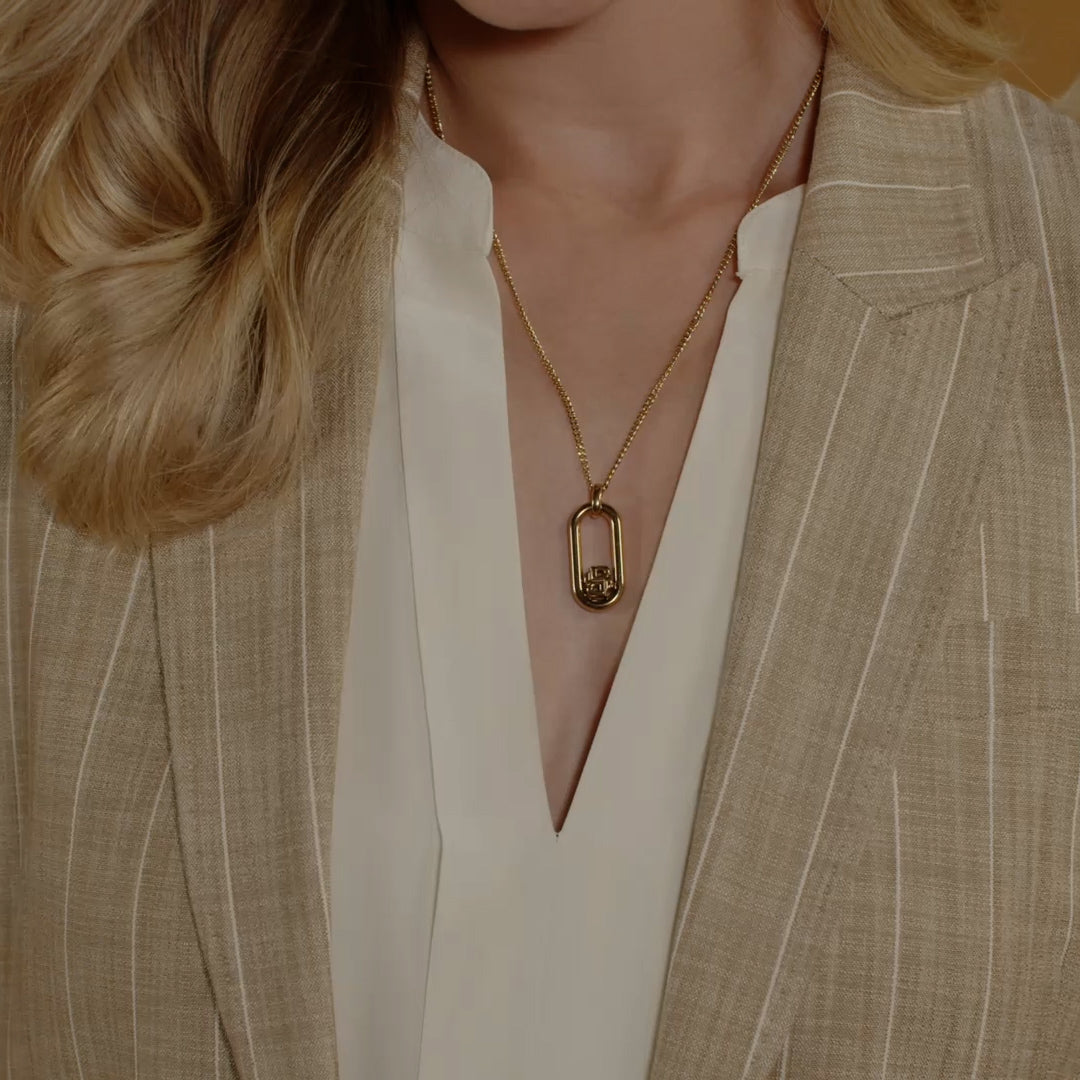 Gold BOSS pendant necklace displayed on model wearing cream blouse and pinstripe blazer, showcasing jewelry styling.