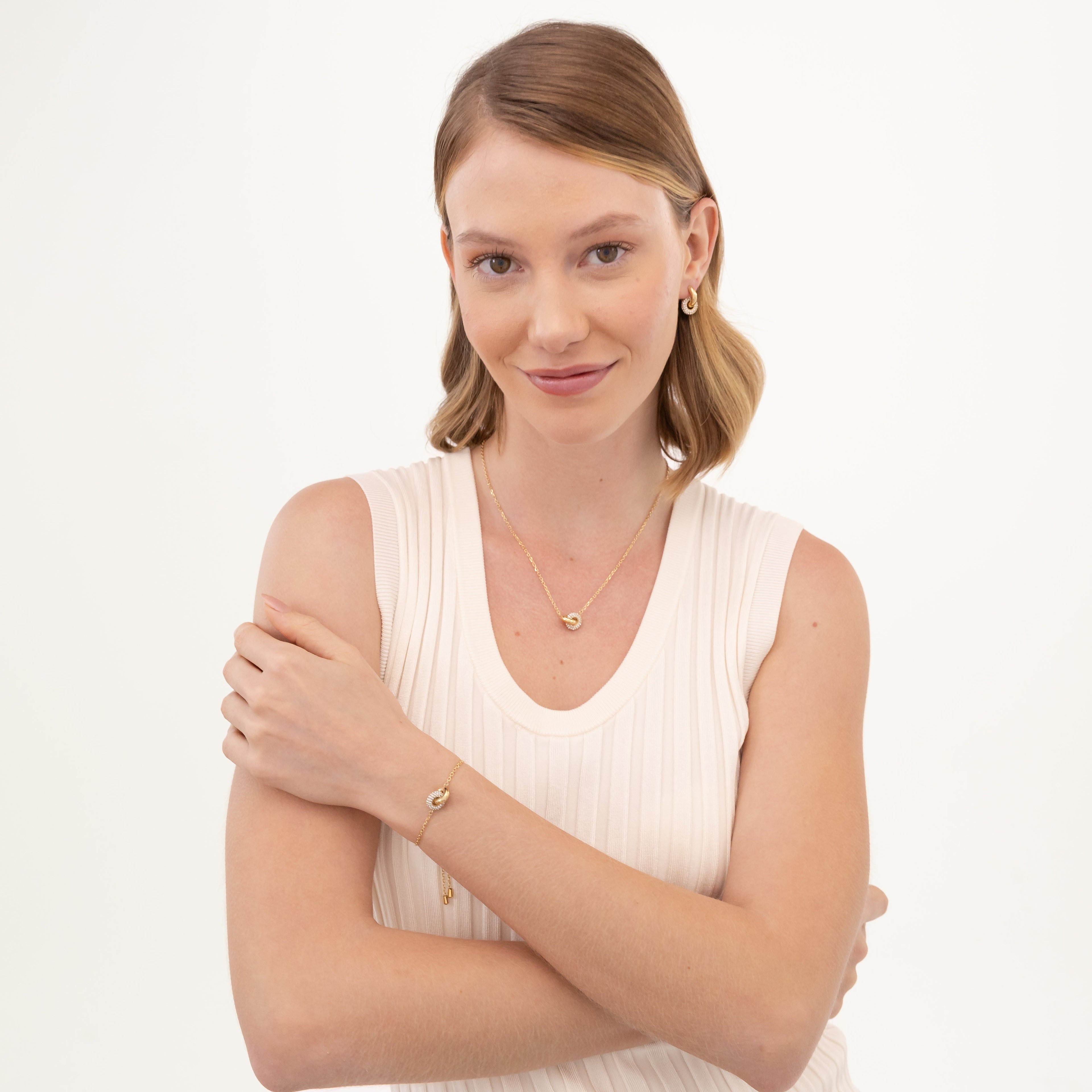 Blonde woman wearing gold jewelry and a white tank top.